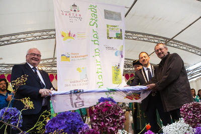 Bild vergr&ouml;&szlig;ern: v.l.n.r.: Roland Albert, Pr&auml;sident der Bayerischen Landesgartenschau GmbH,  Lindauer Bote Hans St&uuml;bner, Stefan Ultsch, B&uuml;rgermeister der Stadt Wassertr&uuml;dingen und Dr. Gerhard Ecker, Oberb&uuml;rgermeister der Stadt Lindau, bei der gemeinsamen Fahnen&uuml;bergabe.